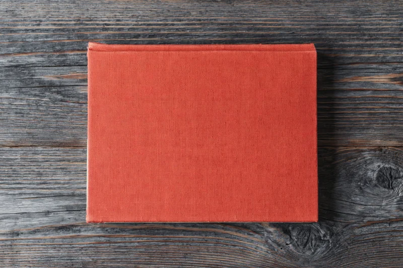 Red hardcover book lying flat on rustic wooden surface