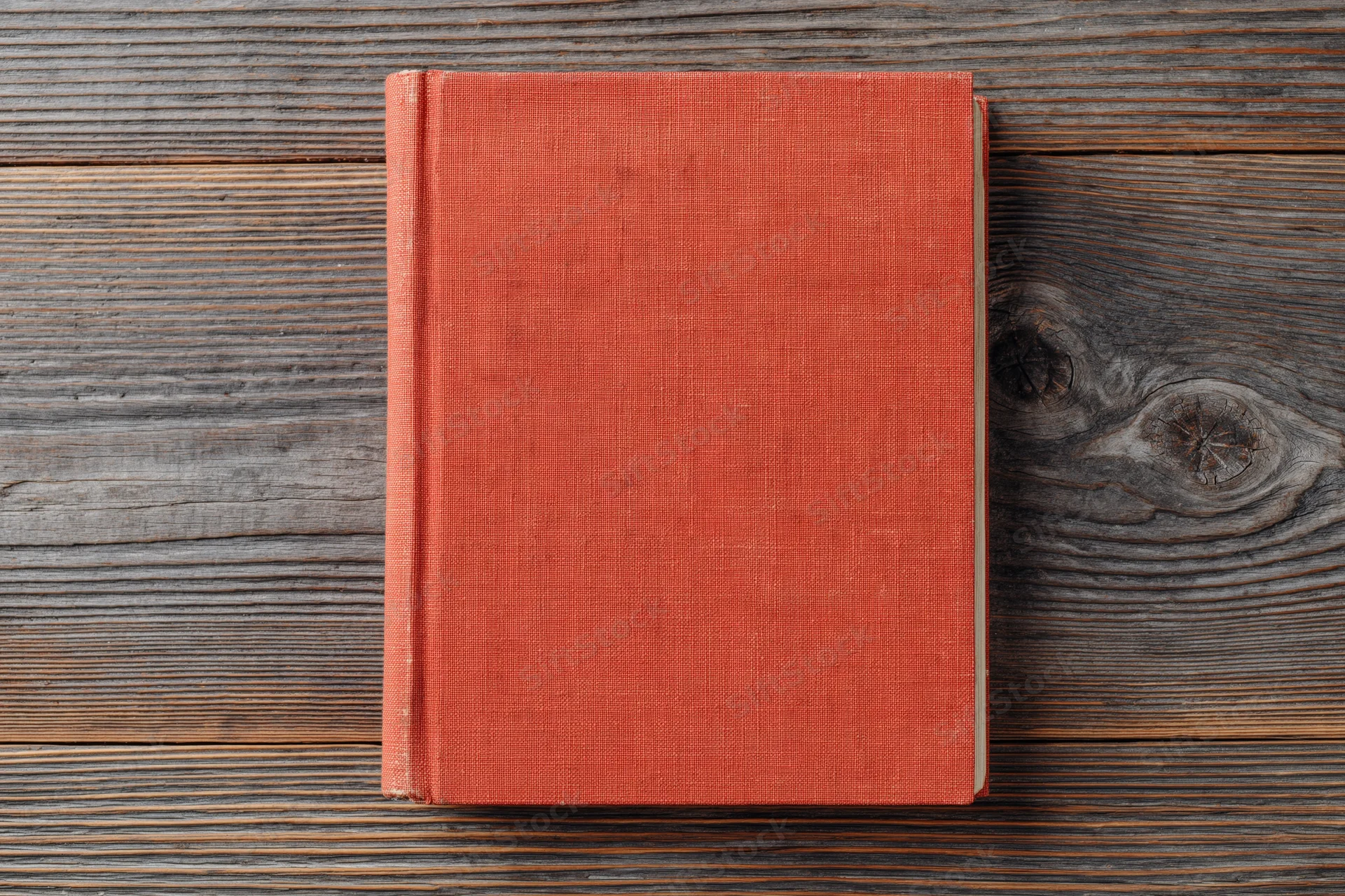 Closed red hardcover book lying flat on rustic wooden surface