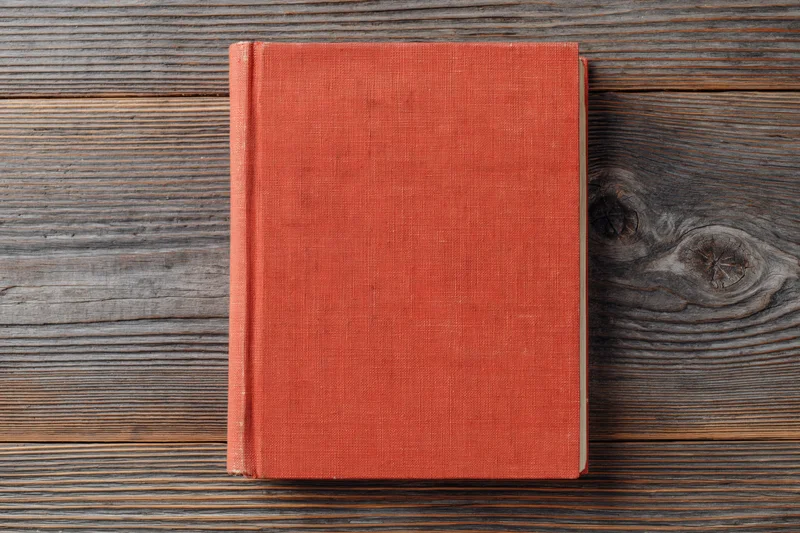 Closed red hardcover book lying flat on rustic wooden surface