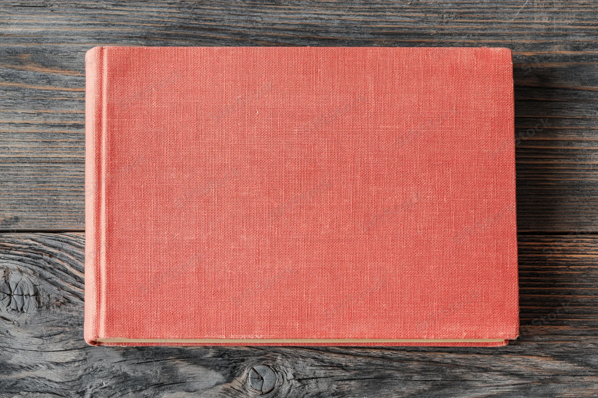 Closed red hardcover book lying flat on rustic wooden surface