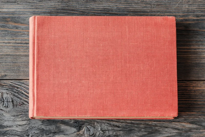 Closed red hardcover book lying flat on rustic wooden surface