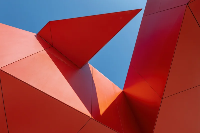 Bold red metal architectural facade with geometric shapes against blue sky