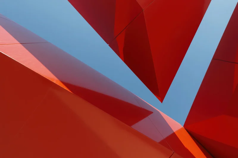 Upward view of bold red metal geometric architecture against blue sky