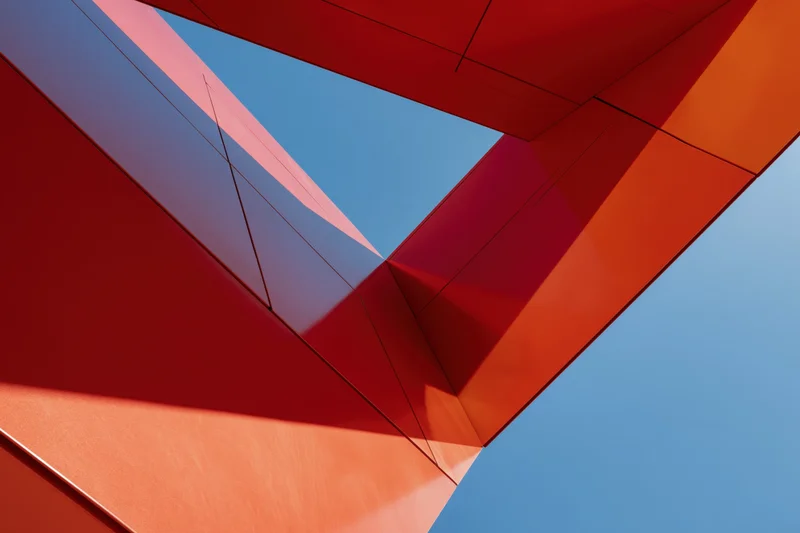 Abstract upward view of bold red metal architectural structure against blue sky