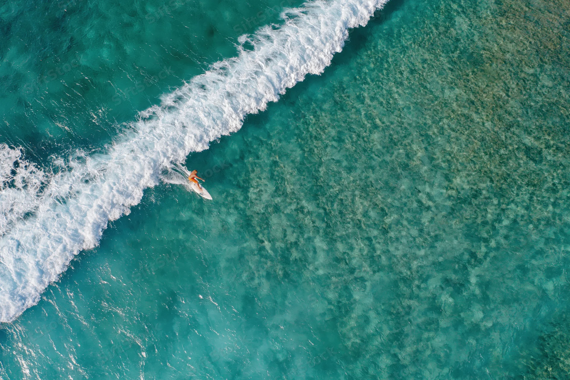 Aerial view of a surfer riding a wave in turquoise ocean water