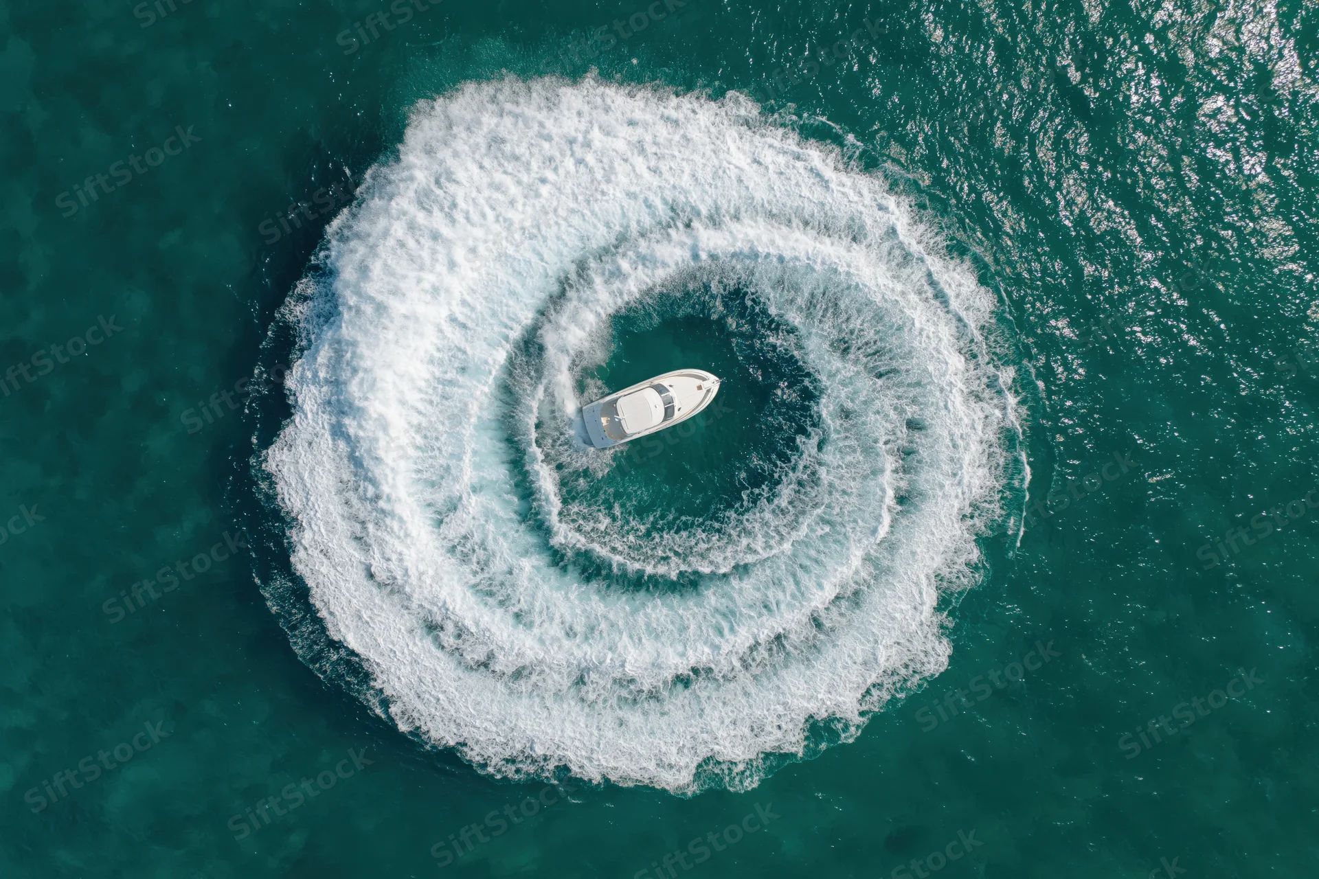 White motorboat circling in the ocean creating a spiral wake from above