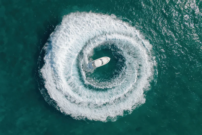 White motorboat circling in the ocean creating a spiral wake from above