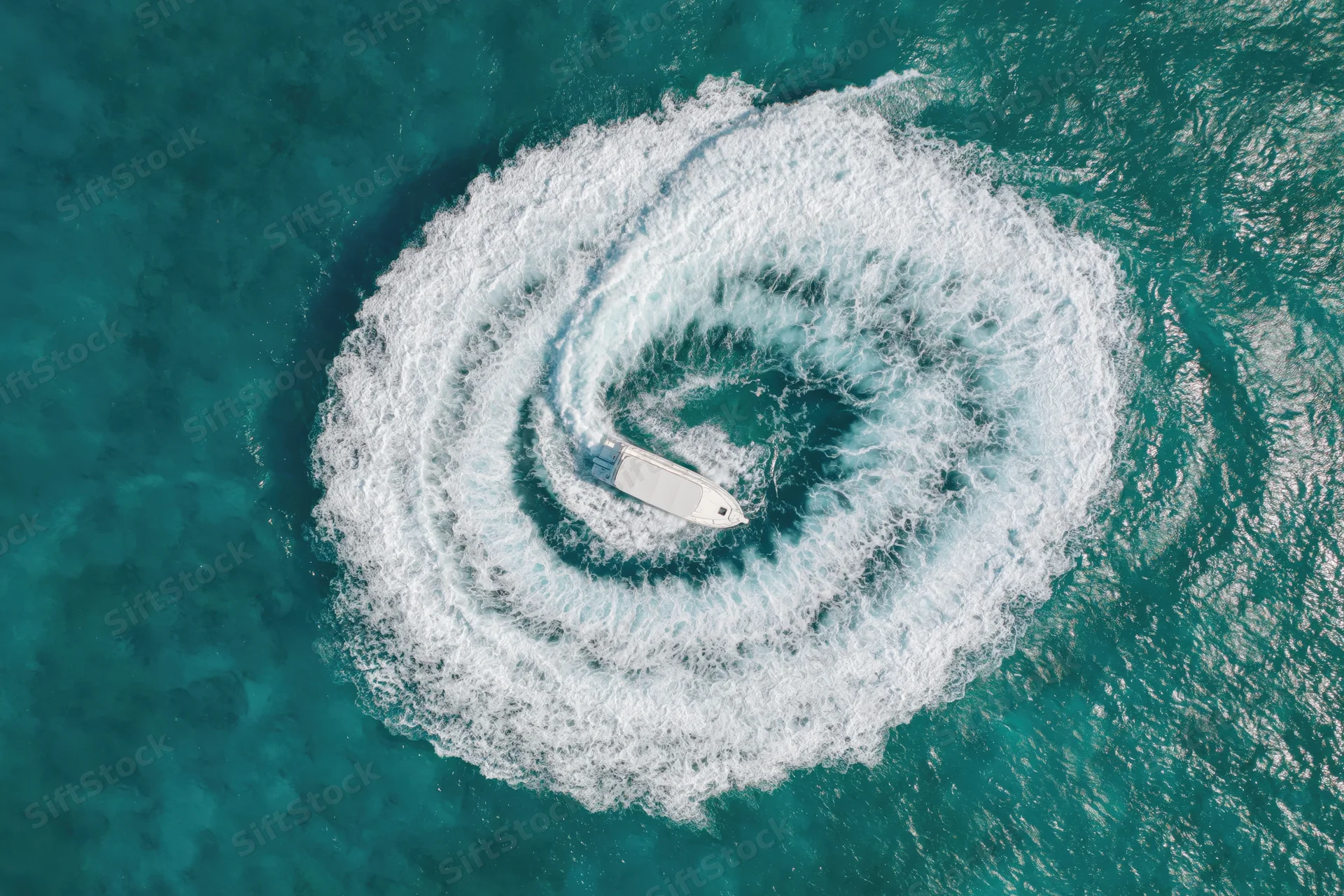 White motorboat creating spiral wake in turquoise ocean viewed from above