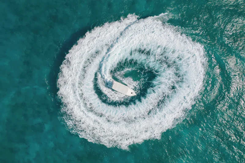 White motorboat creating spiral wake in turquoise ocean viewed from above