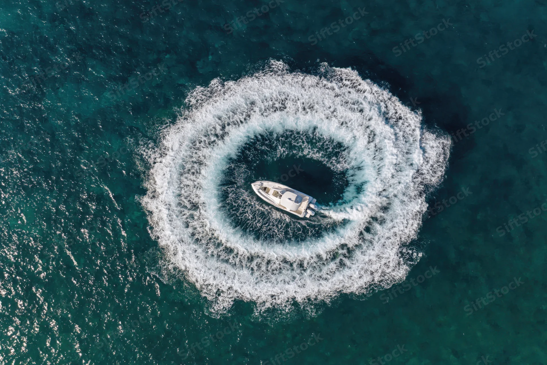 White motorboat circling in the ocean creating a circular wake from an aerial view
