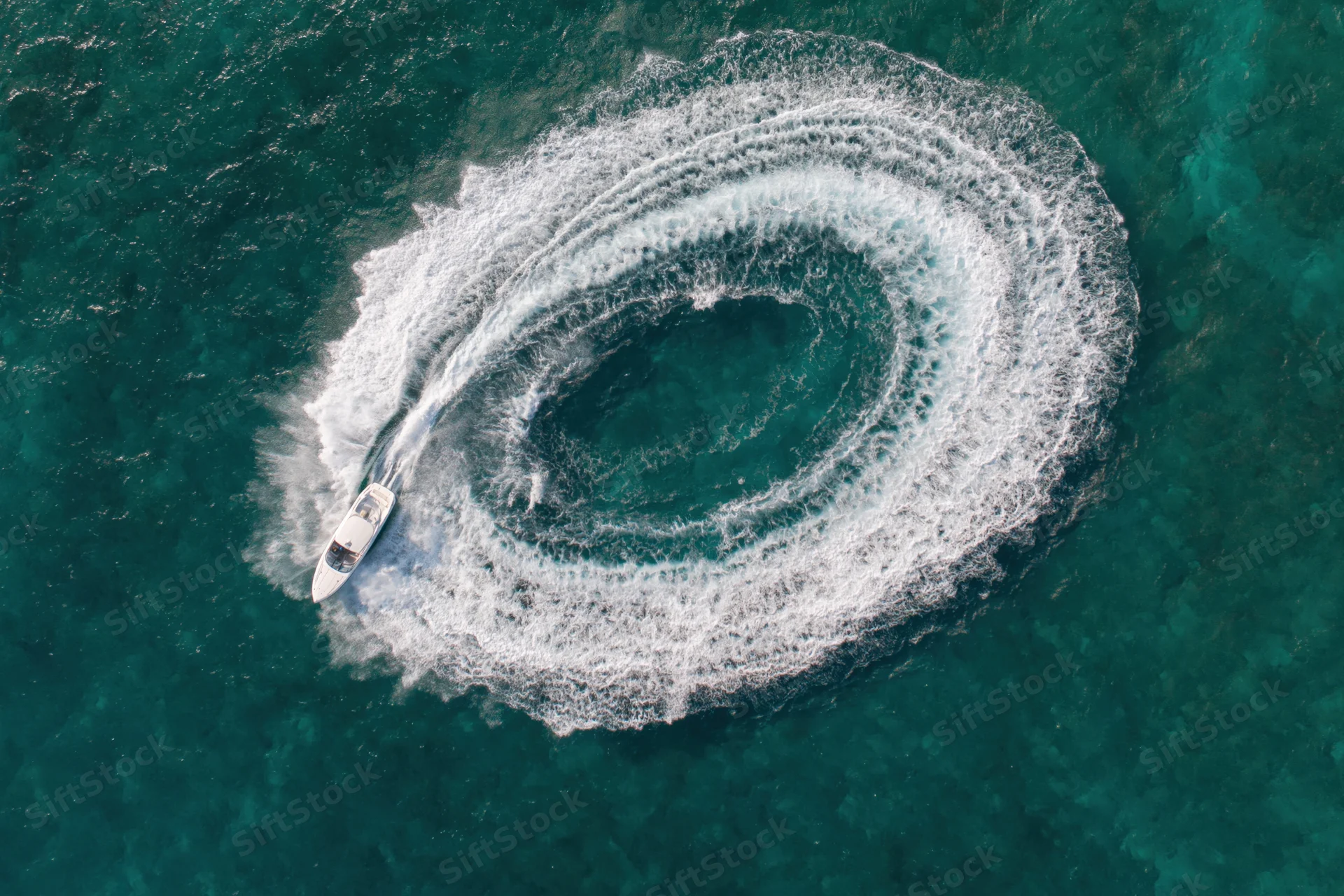 White motorboat circling in the ocean creating a spiral wake from an aerial view