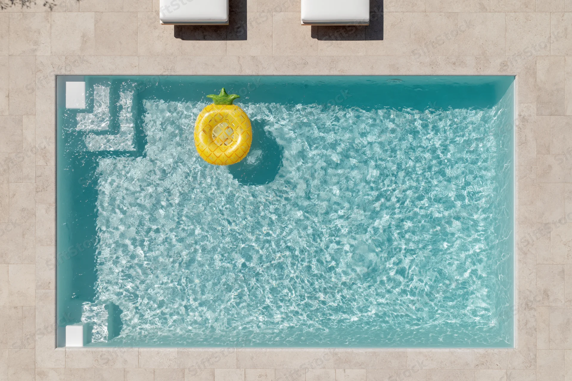 Aerial overhead view of rectangular outdoor swimming pool with yellow pineapple inflatable float and beige tiled patio