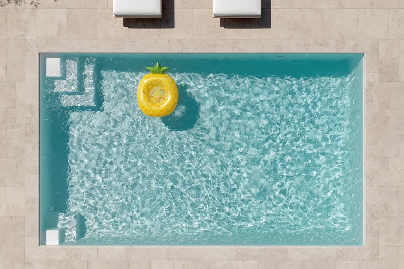 Aerial overhead view of rectangular outdoor swimming pool with yellow pineapple inflatable float and beige tiled patio