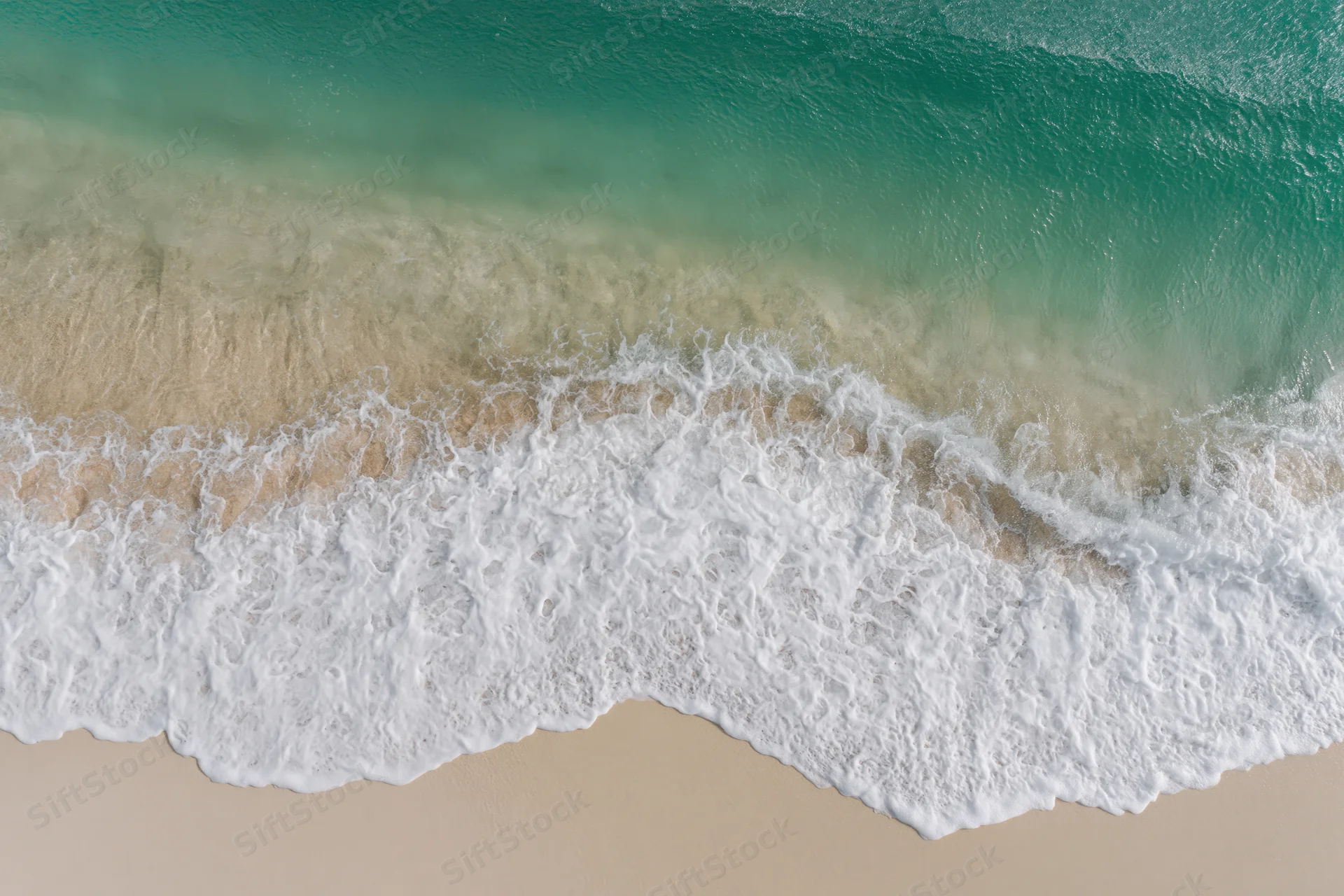 Aerial top-down view of a gentle ocean wave washing onto a sandy beach