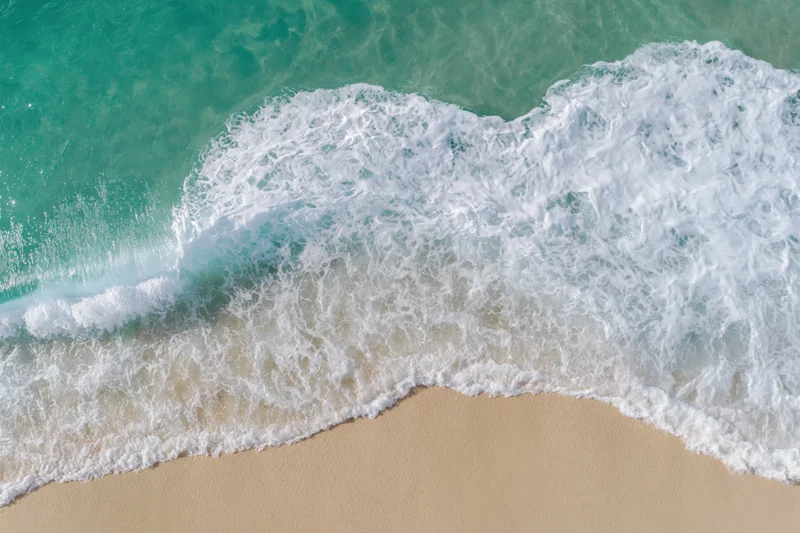 Aerial top-down view of a gentle ocean wave washing onto clear sandy beach