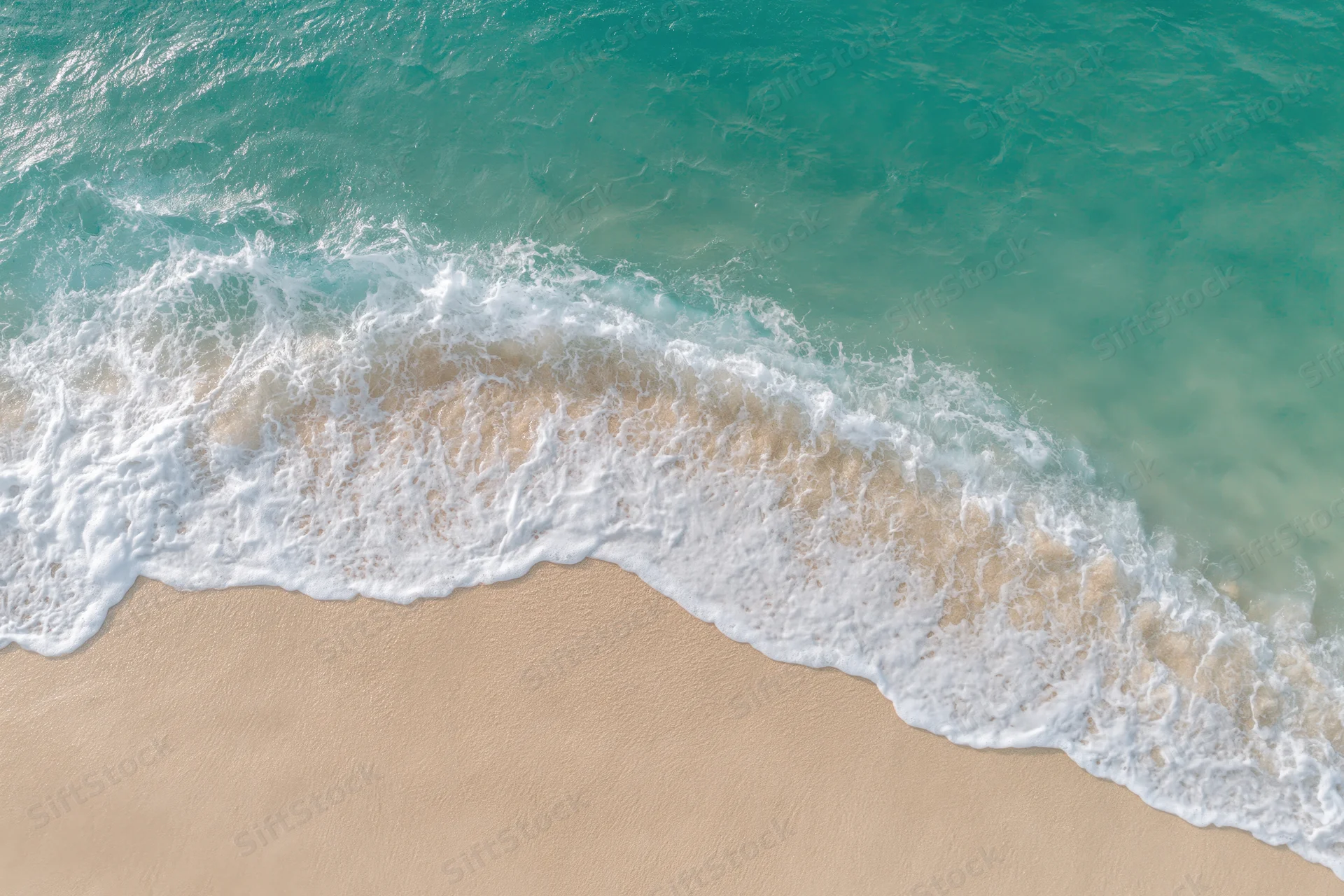 Aerial top-down view of a gentle ocean wave washing onto a sandy beach