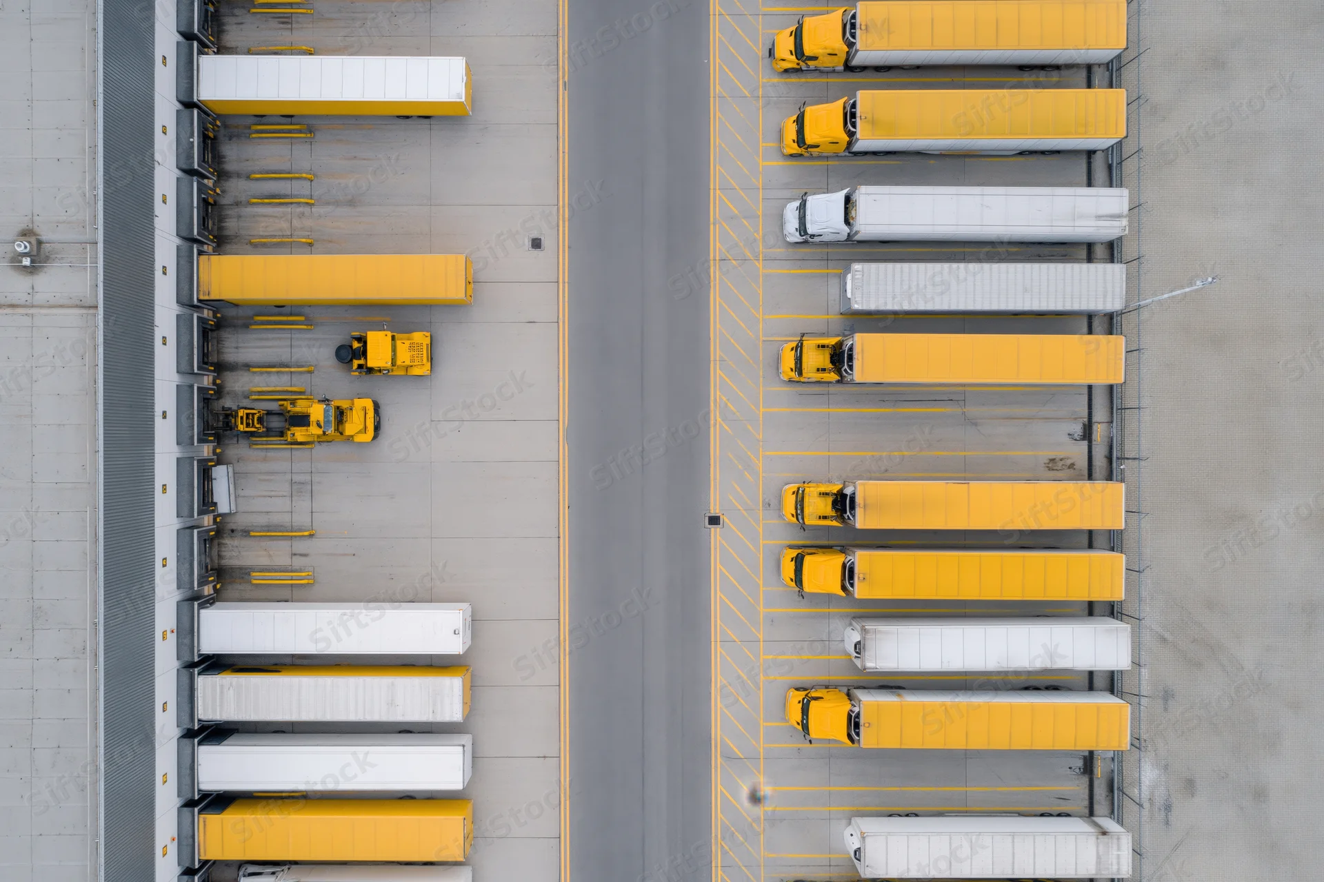 Aerial top-down view of logistics depot with rows of yellow and white trucks parked at loading docks and in parking lanes