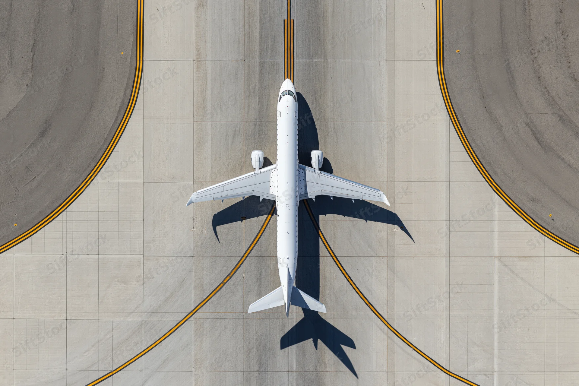 White commercial passenger jet taxiing on airport tarmac from overhead view