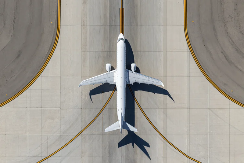 White commercial passenger jet taxiing on airport tarmac from overhead view