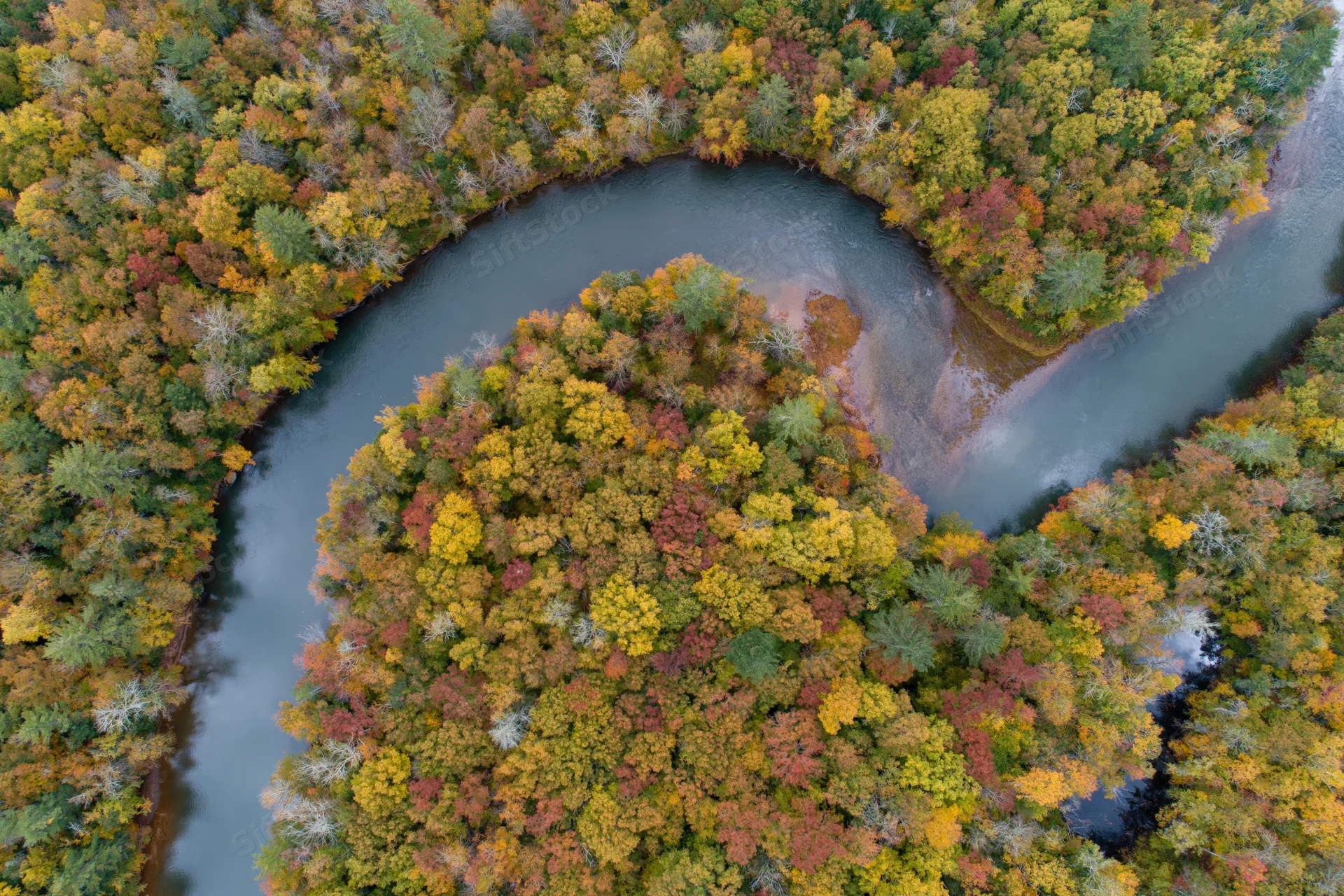 Aerial top-down view of a winding river curving through autumn forest canopy