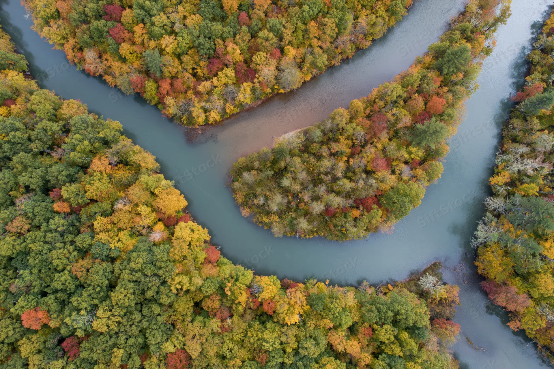 Aerial view of a winding river curving through autumn forest canopy