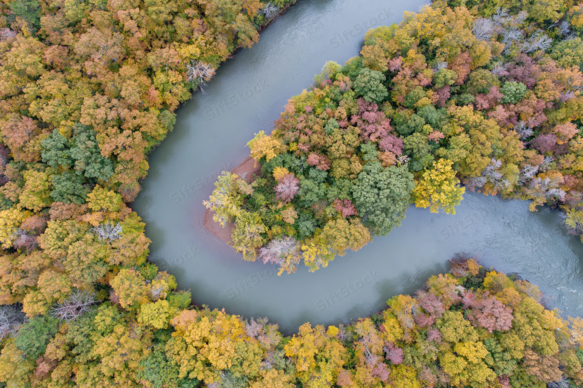 Aerial top-down view of a winding river curving through autumn forest canopy