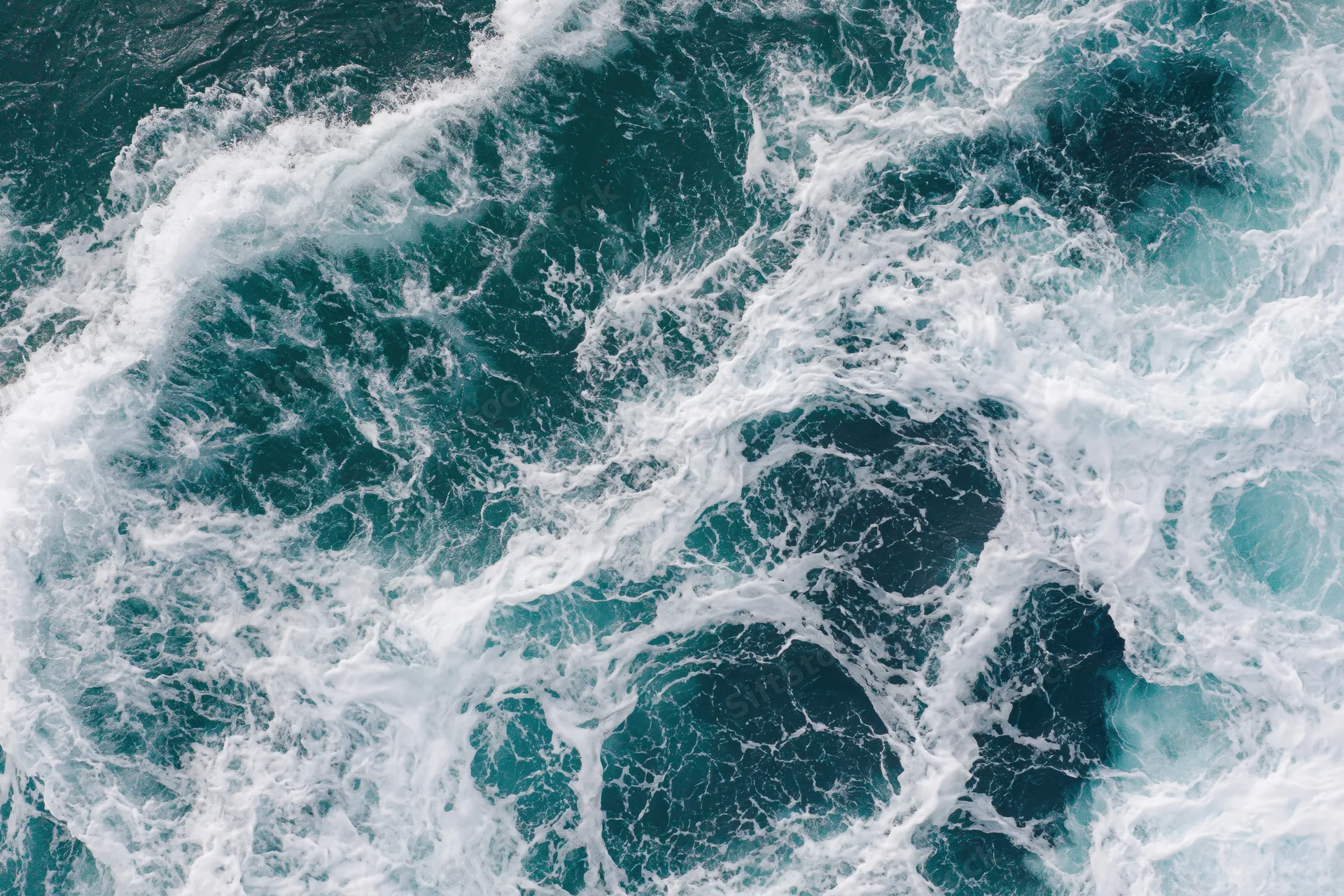 Top-down view of churning deep ocean waves with white foam and swirling turquoise water