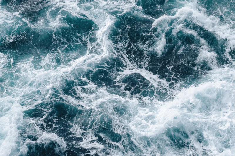 Top-down view of churning deep ocean water with white foam and swirling waves