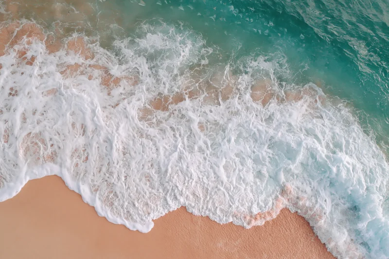 Aerial top-down view of gentle ocean waves washing onto a wide sandy beach