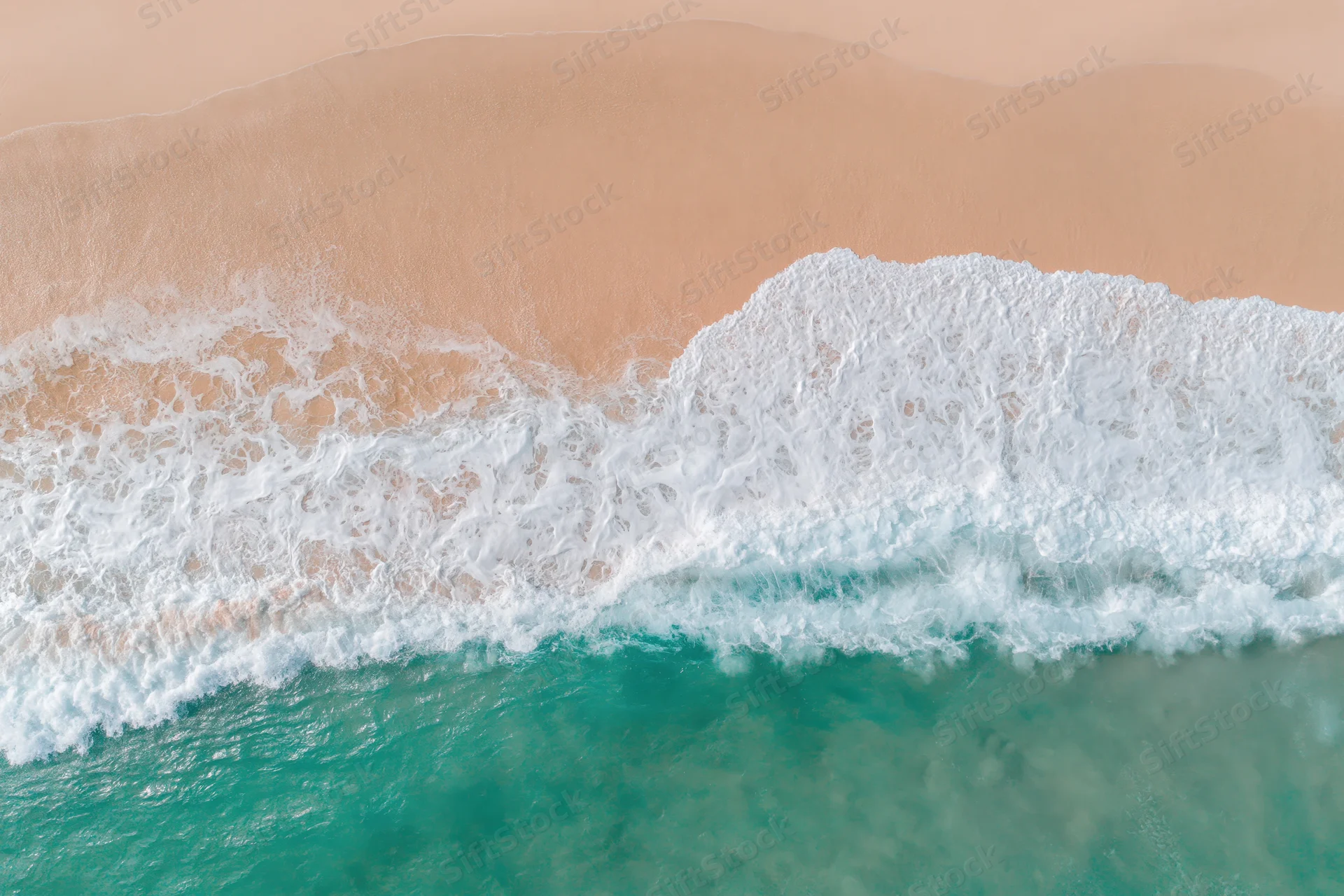 Aerial top-down view of gentle ocean waves washing onto a wide sandy beach
