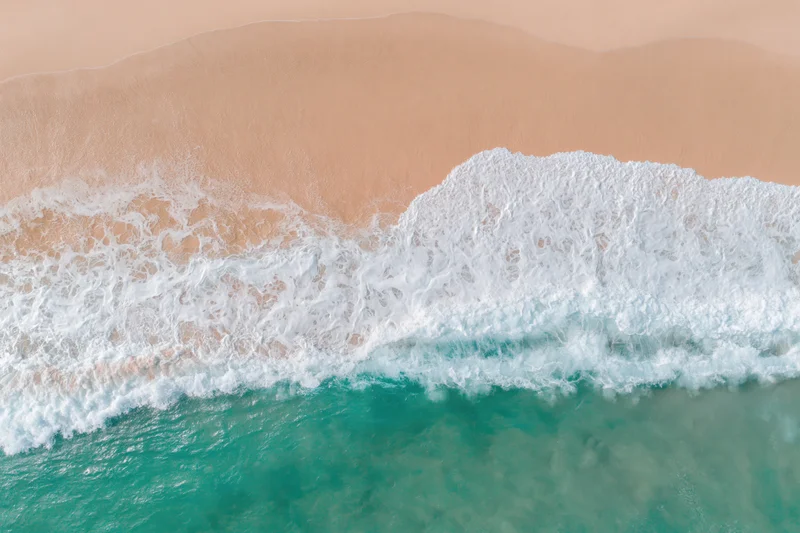 Aerial top-down view of gentle ocean waves washing onto a wide sandy beach