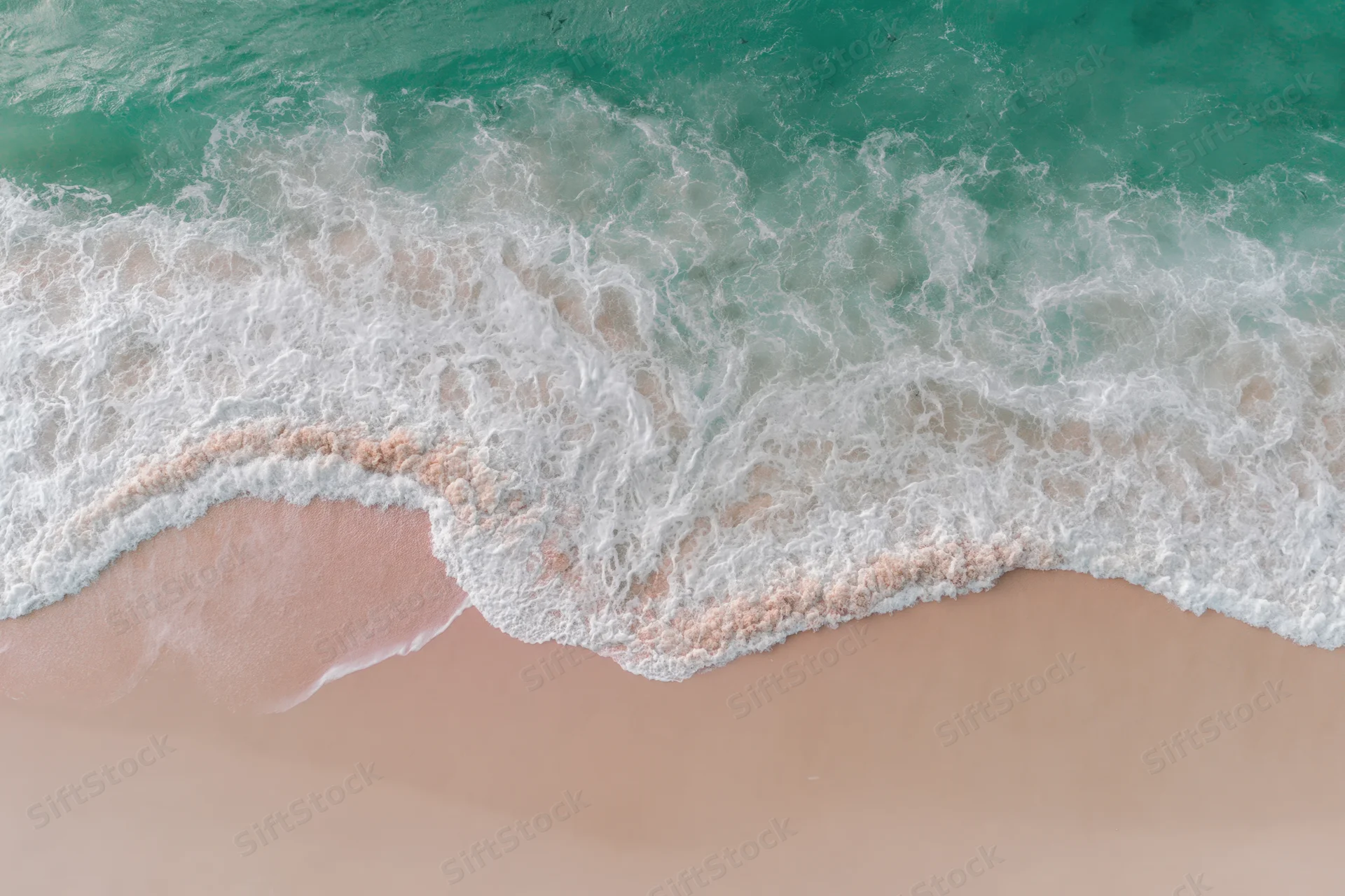 Aerial top-down view of gentle ocean waves washing onto a wide sandy beach