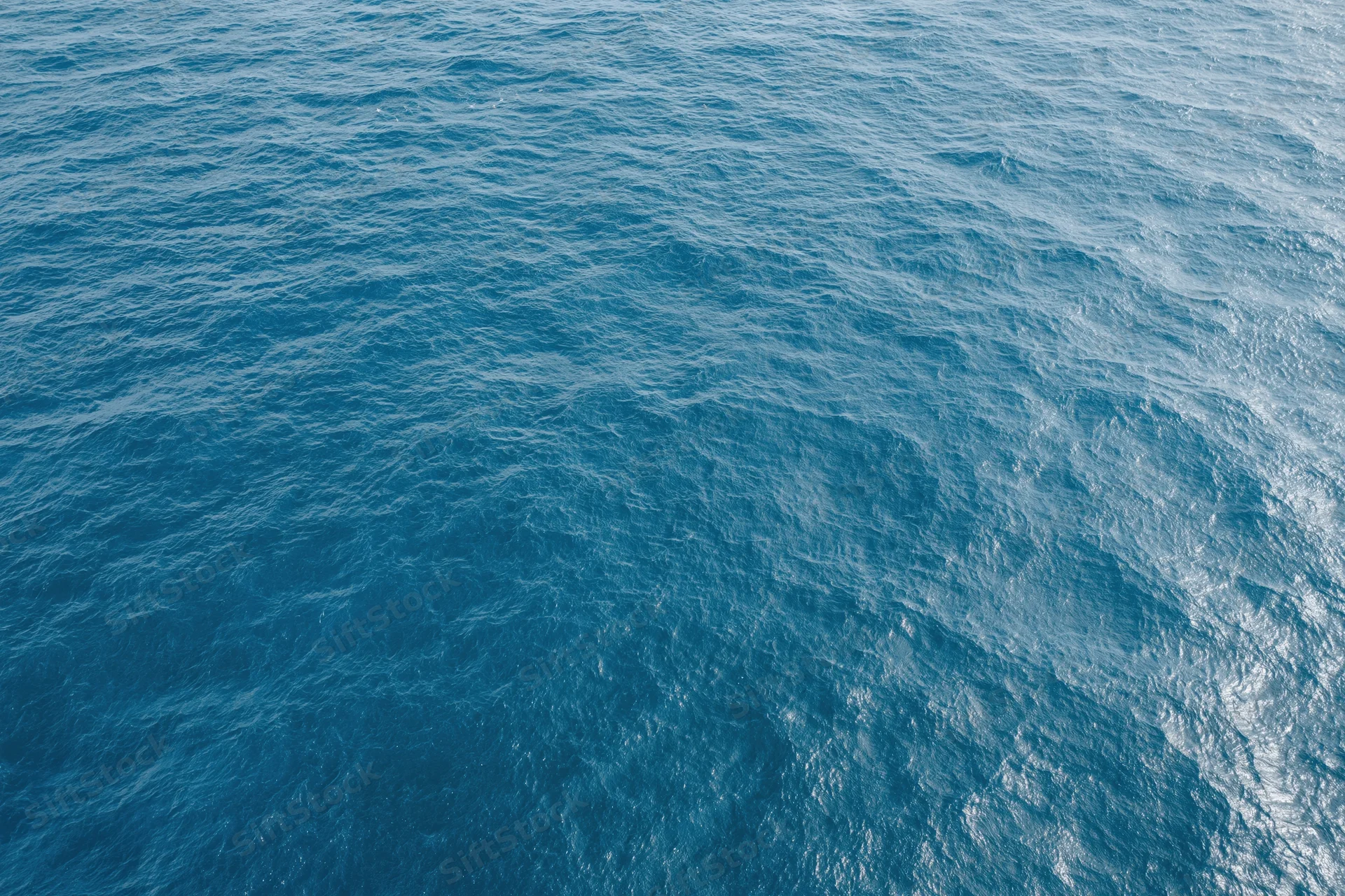 Aerial top-down view of open ocean surface with gentle ripples and light reflections