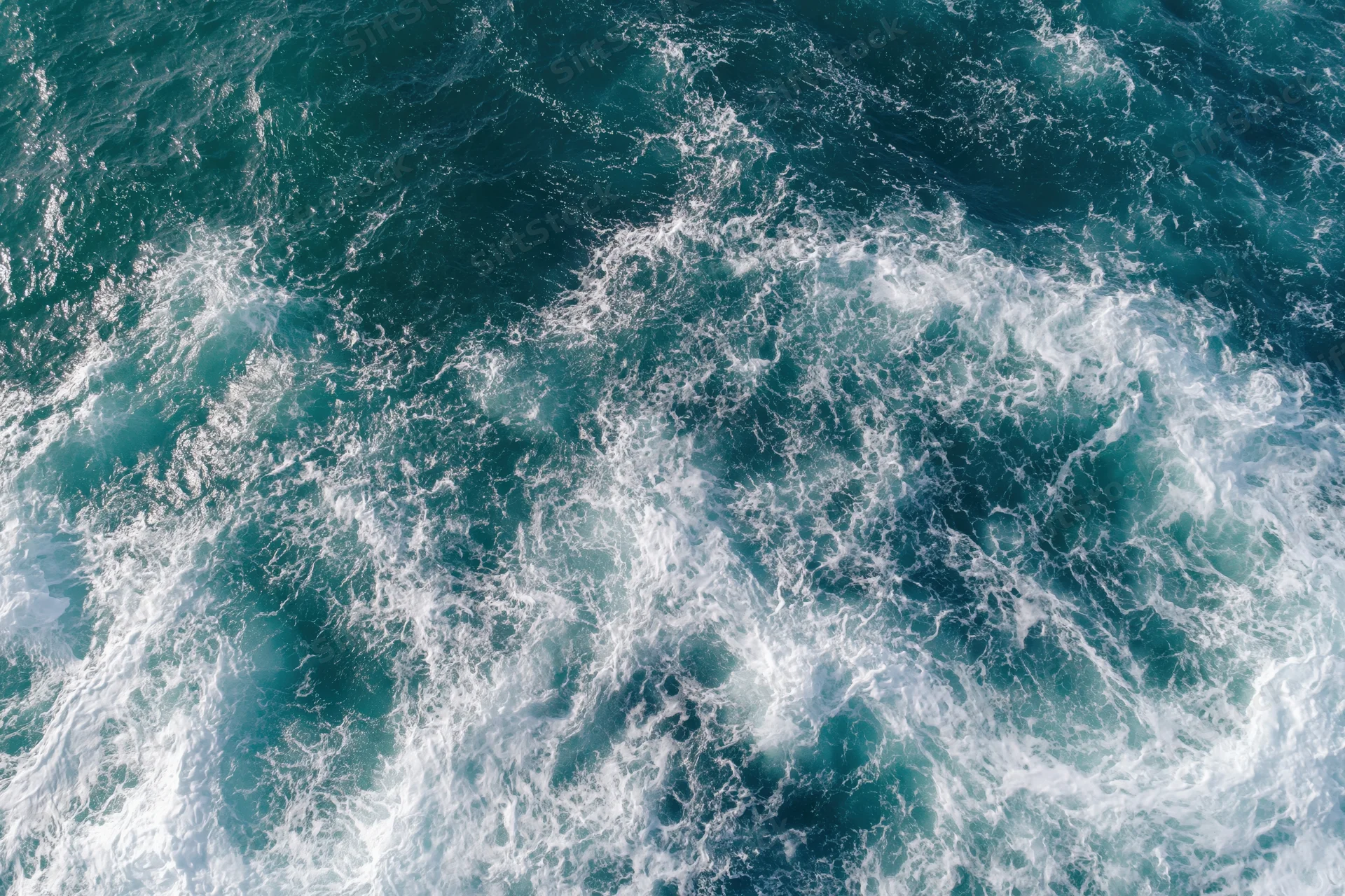 Aerial top-down view of open ocean surface with scattered white foam and swirling waves