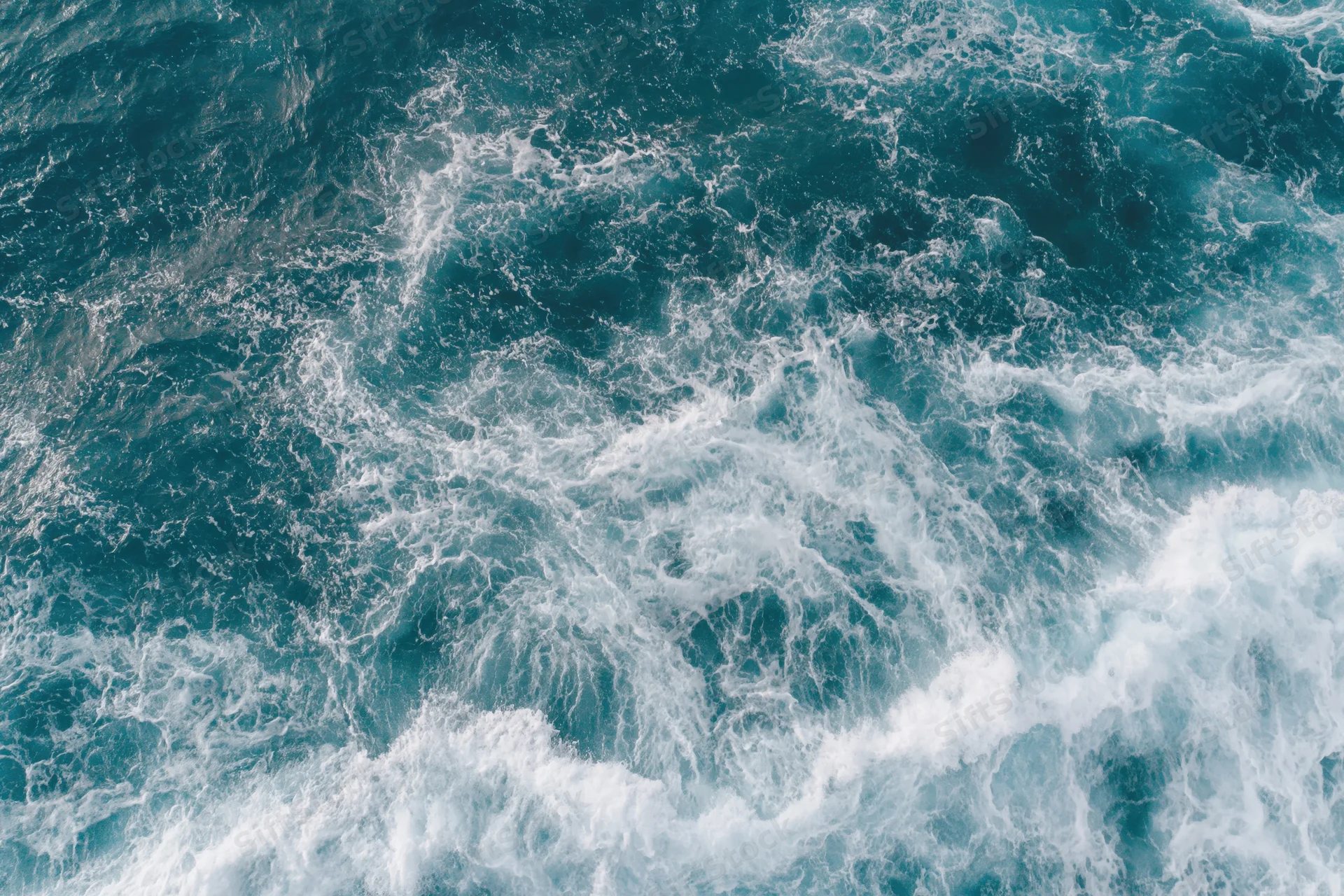 Top-down view of turbulent ocean surface with white foam and blue waves