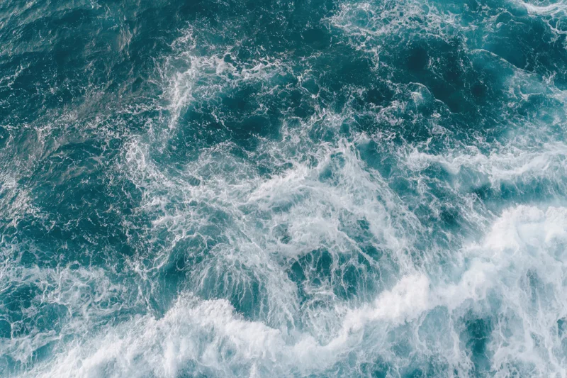 Top-down view of turbulent ocean surface with white foam and blue waves