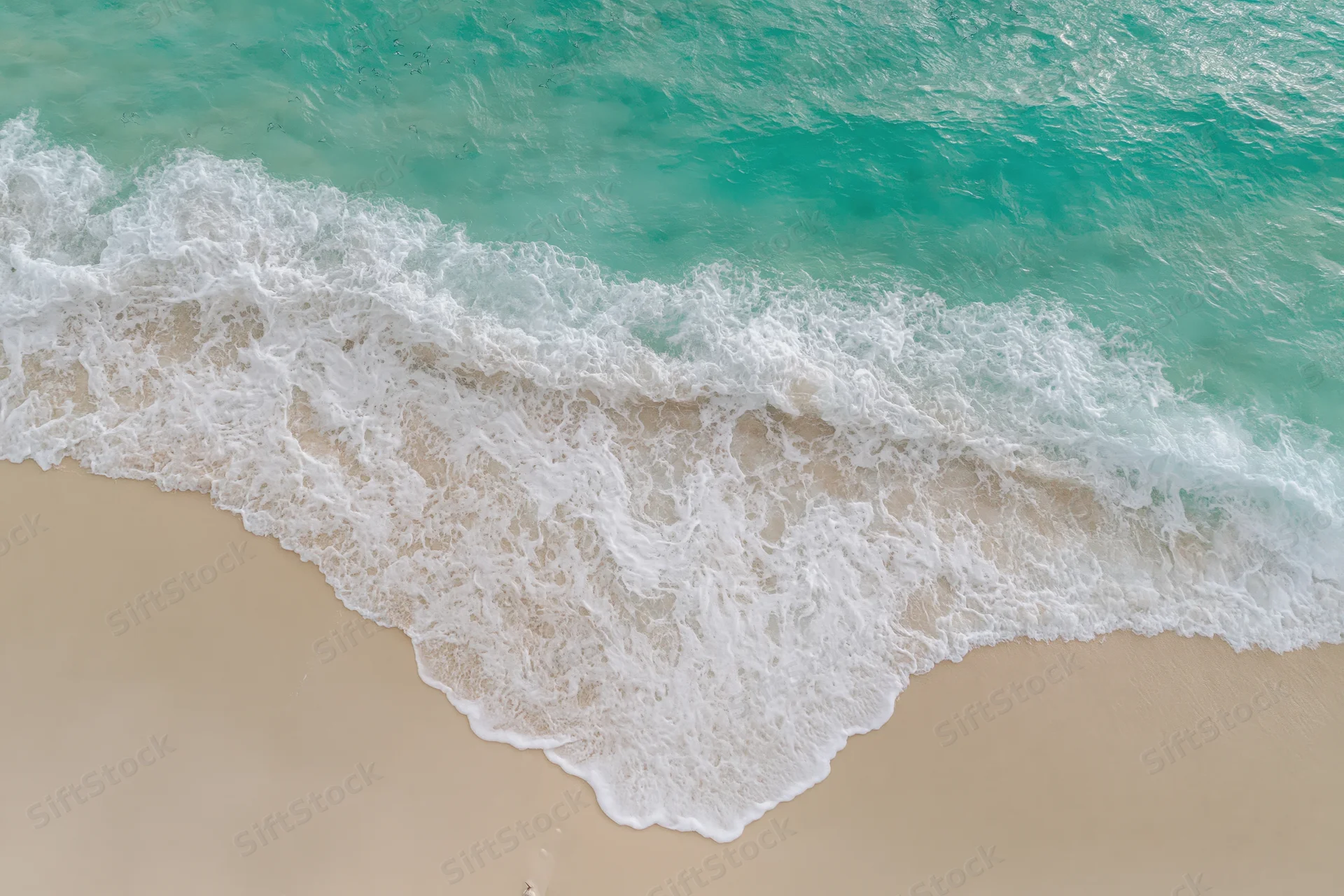 Aerial top-down view of turquoise ocean waves washing over sandy beach