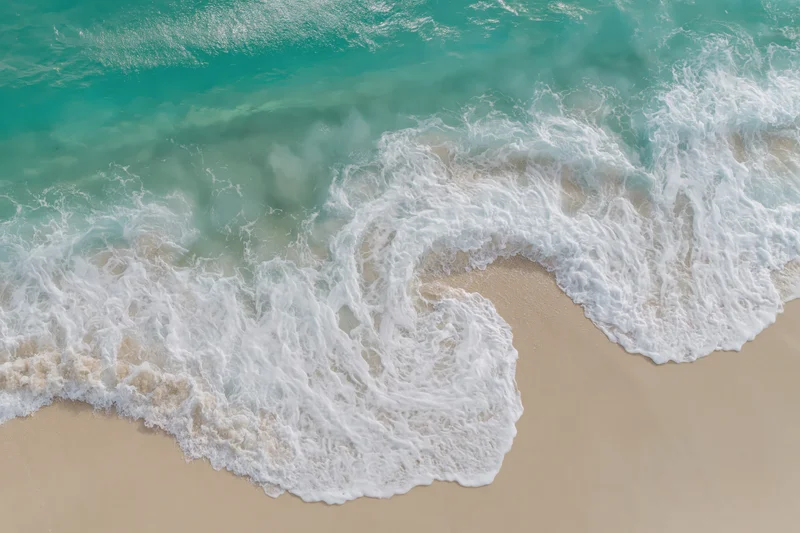 Aerial top-down view of turquoise ocean waves washing over sandy beach