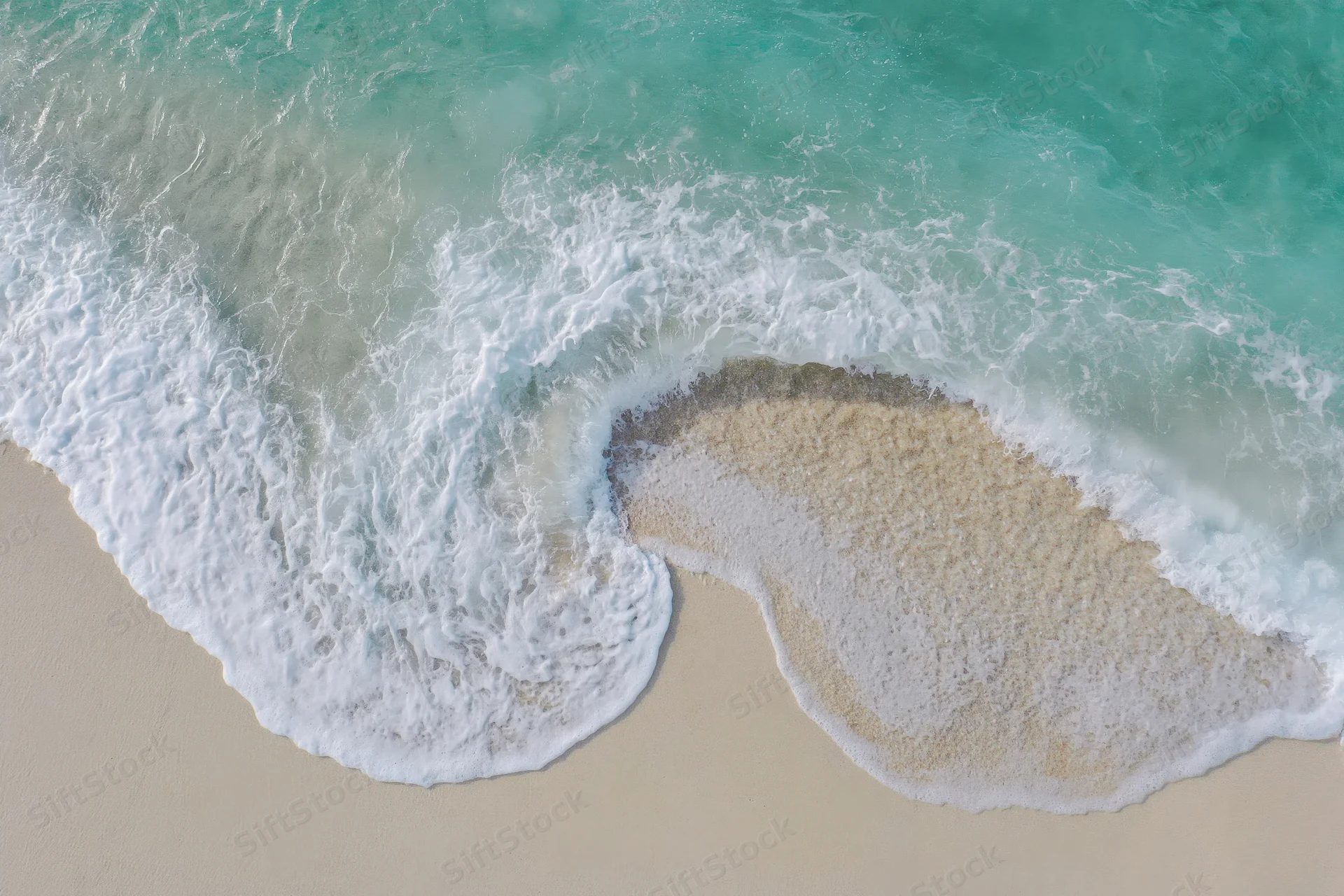 Aerial top-down view of ocean waves washing over sandy beach