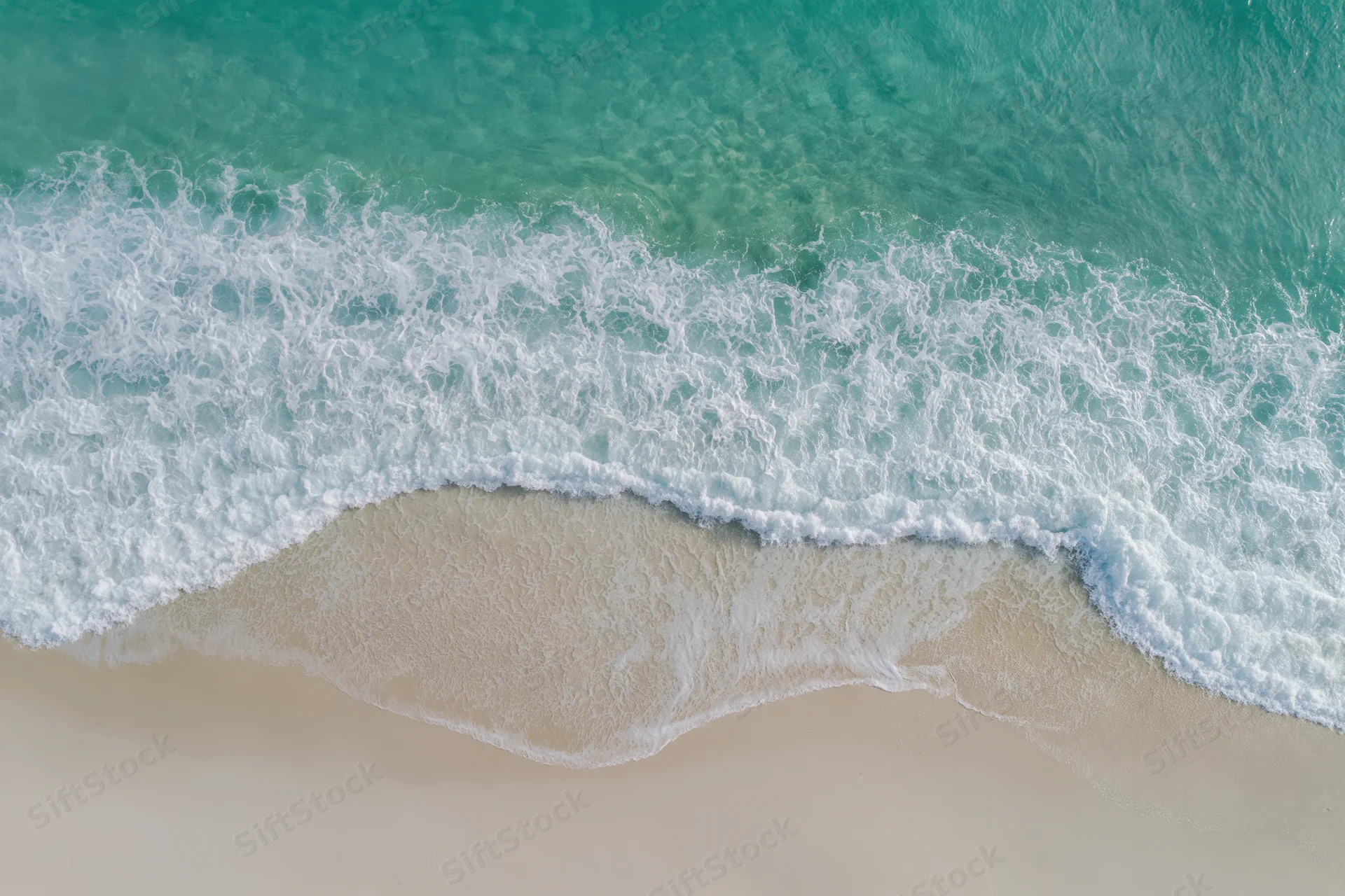 Aerial top-down view of ocean waves washing over sandy beach