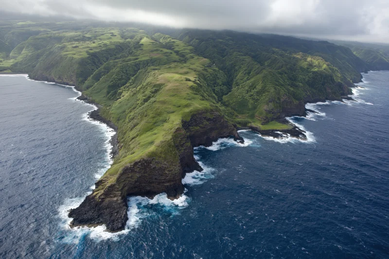 Aerial view of rugged volcanic coastline with green cliffs meeting ocean waves