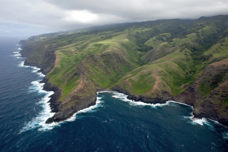 Aerial view of rugged volcanic coastline with steep green cliffs meeting the ocean