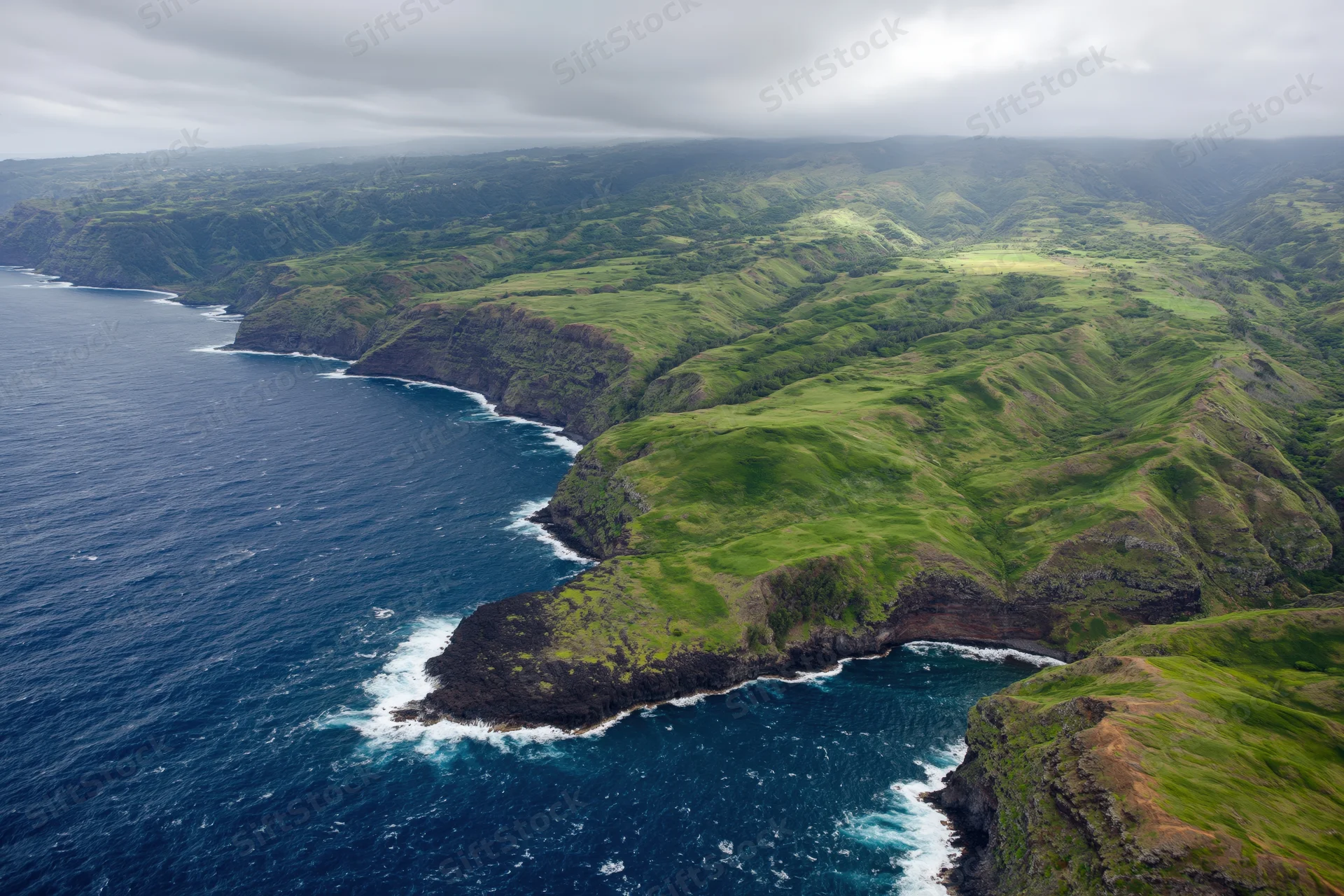 Aerial view of rugged volcanic coastline with green hills meeting the ocean