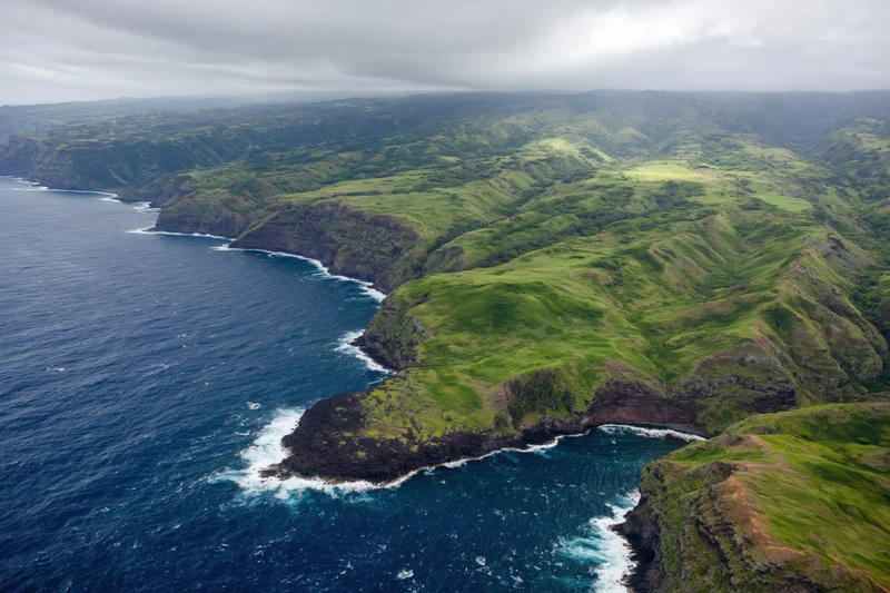 Aerial view of rugged volcanic coastline with green hills meeting the ocean