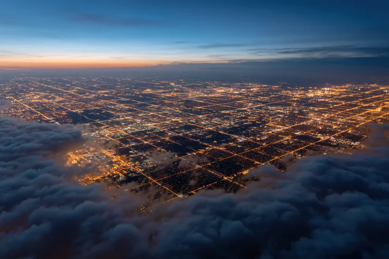 Aerial view of a sprawling city at night from high altitude above clouds