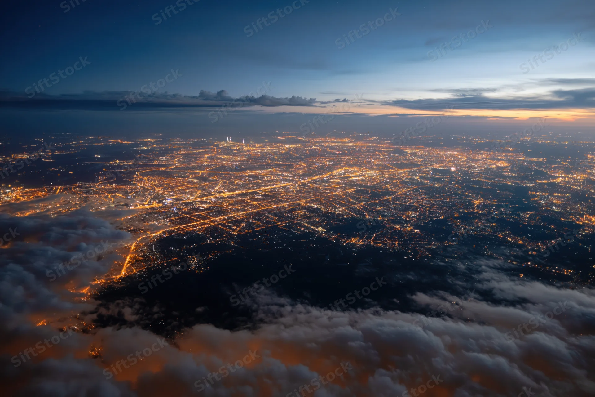 Aerial view of a sprawling city at night from high altitude above clouds