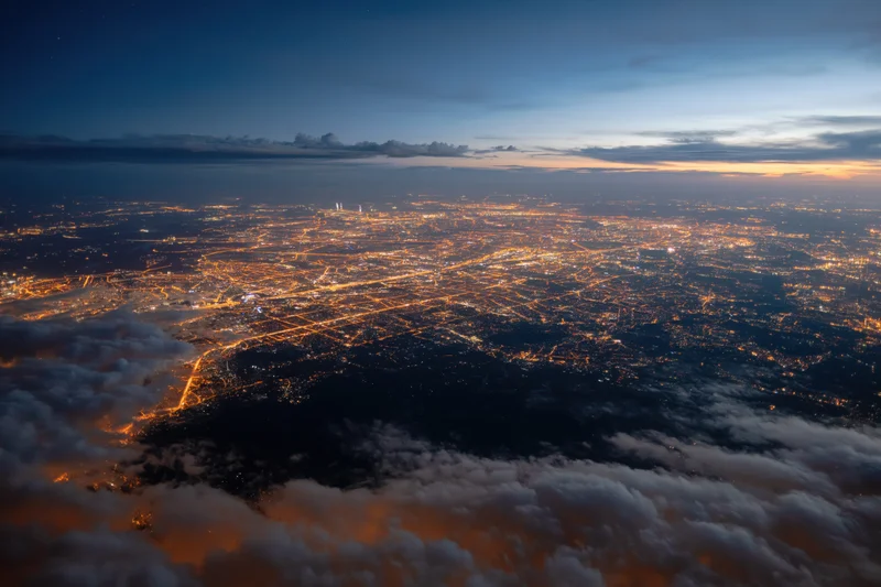 Aerial view of a sprawling city at night from high altitude above clouds