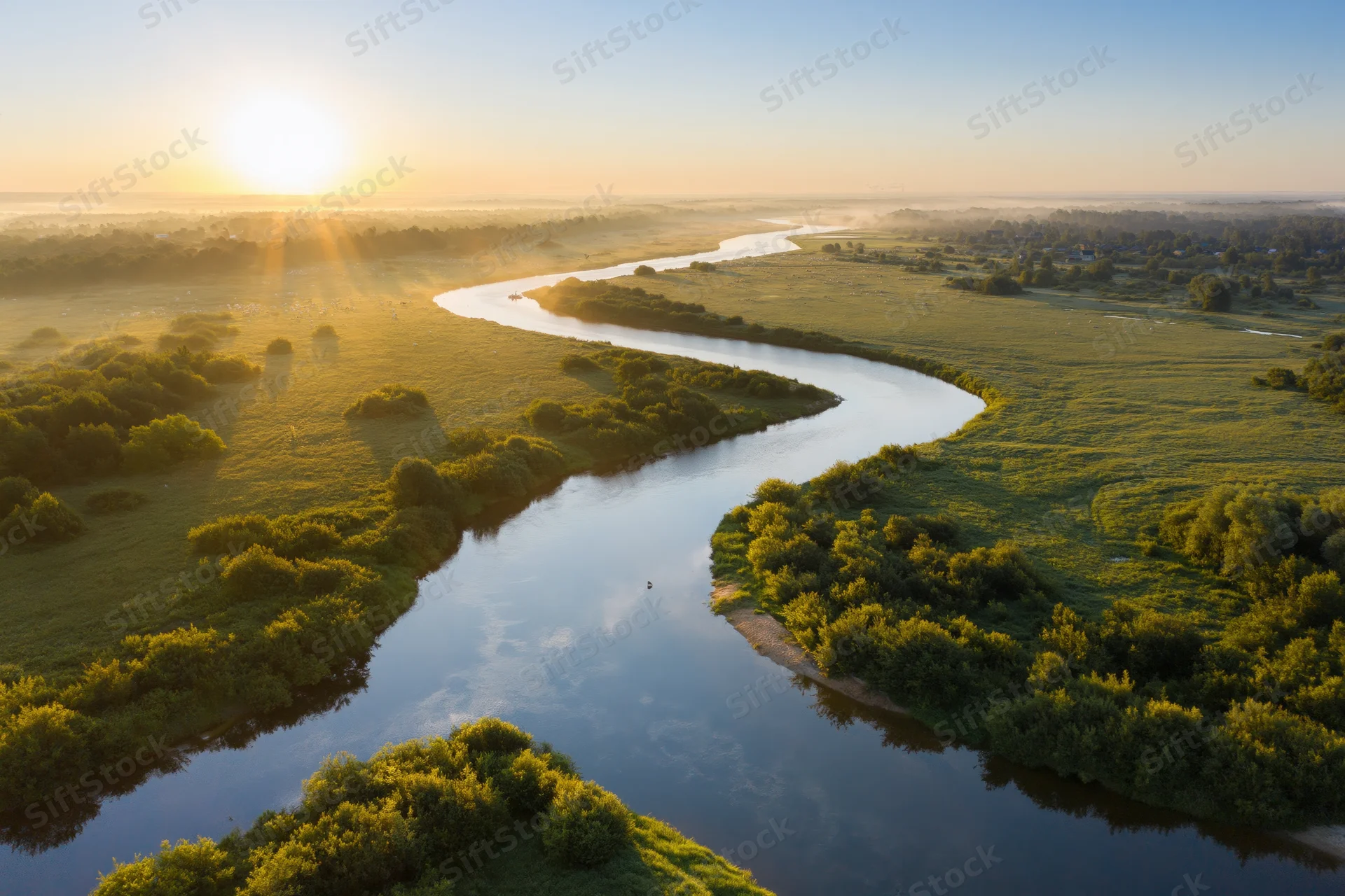 Aerial view of a winding river meandering through flat green wetlands at sunrise