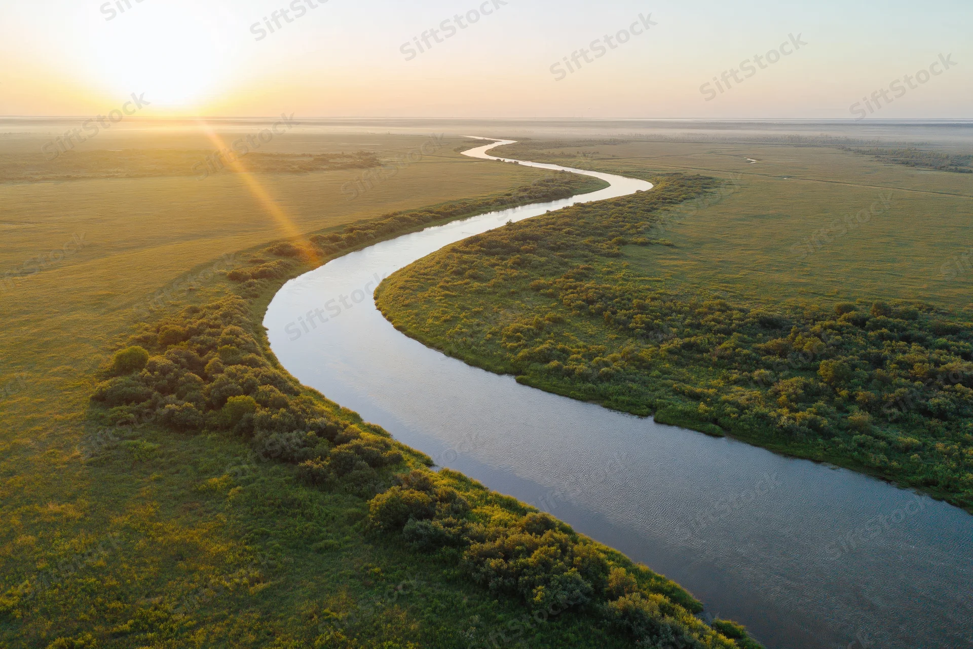 Aerial view of a winding river snaking through flat green wetlands at sunset