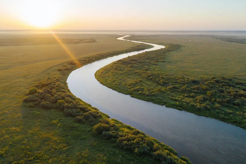 Aerial view of a winding river snaking through flat green wetlands at sunset